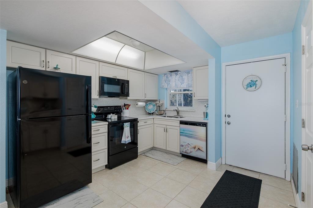 A kitchen features white cabinets, black appliances, light tile flooring, and a blue-painted wall — 4939 FLORAMAR TERRACE UNIT 312, NEW PORT RICHEY, FL