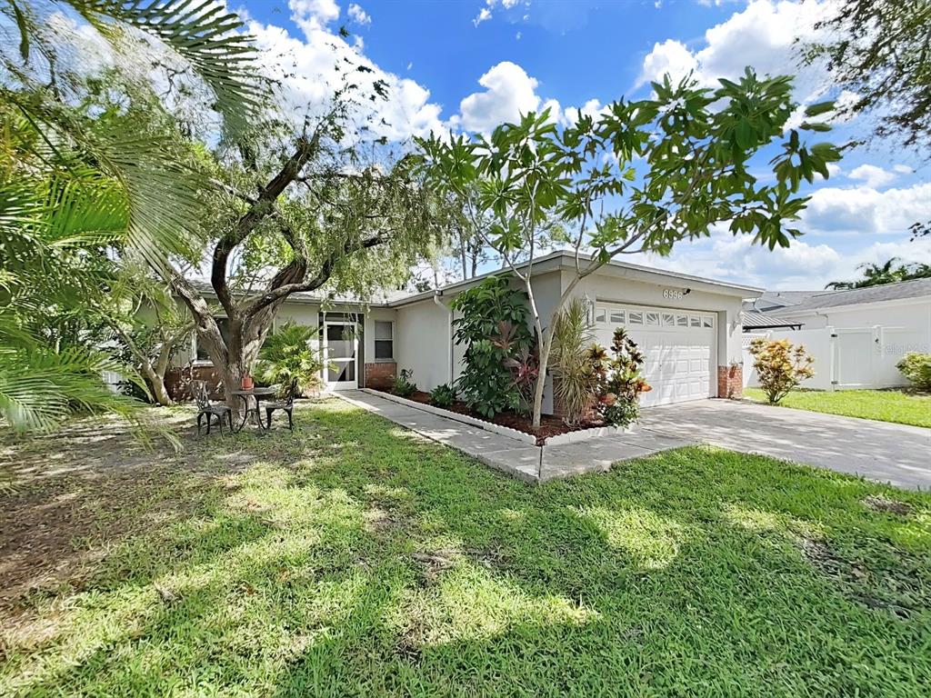 A single-story house with a white garage, a front walkway, and a large shade tree — 6996 122ND DRIVE, LARGO, FL