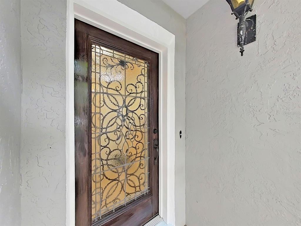 A dark wood front door with decorative leaded glass sits in a light-colored stucco entryway — 6996 122ND DRIVE, LARGO, FL