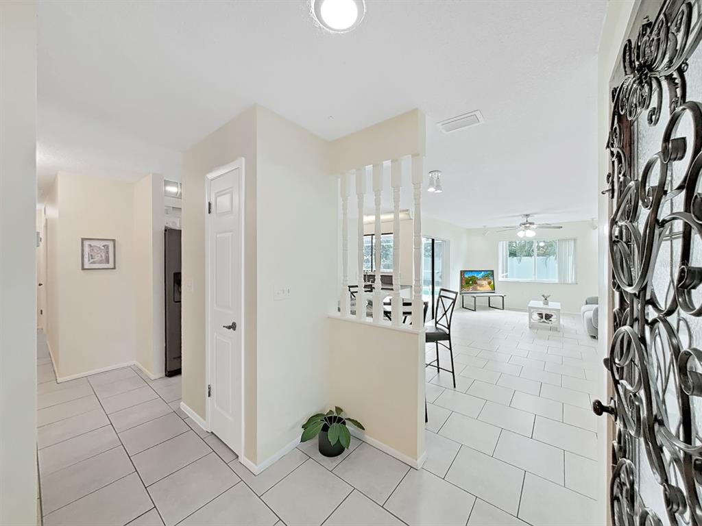 An entryway with light tile flooring leads into an open-concept living area with white spindles — 6996 122ND DRIVE, LARGO, FL