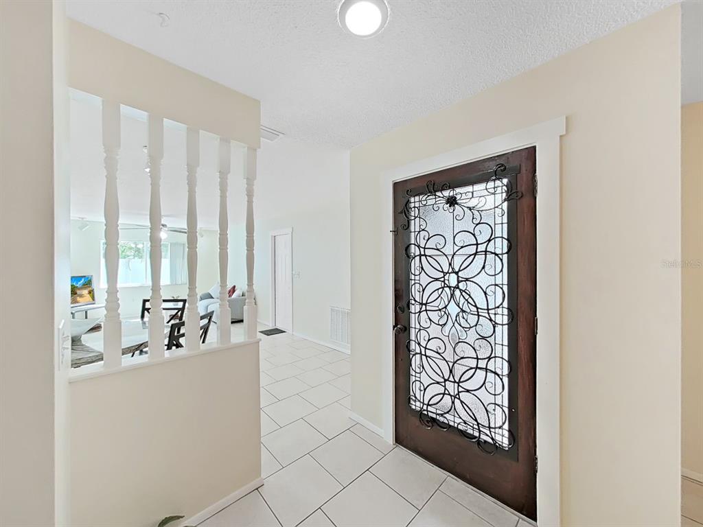 An entryway features white tile flooring, a decorative iron-grille door, and a white spindle partition — 6996 122ND DRIVE, LARGO, FL