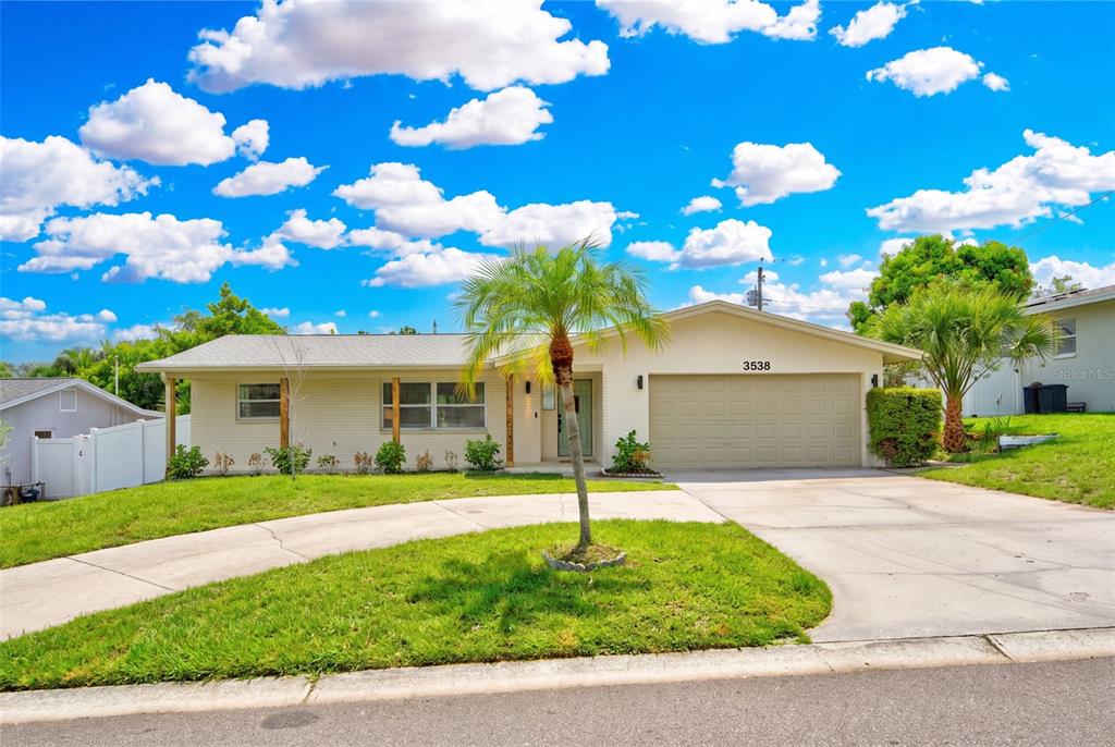 A single-story house with a light-colored brick facade, a two-car garage, and a palm tree — 3538 SHADY BLUFF DRIVE, LARGO, FL