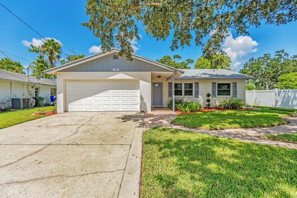 A single-story house with a white garage, gray front door, and a paved walkway — 1788 PATRICIA AVENUE, DUNEDIN, FL