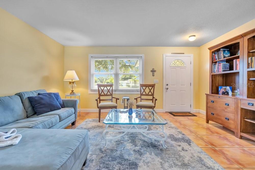 A living room features a blue sectional sofa, two wooden chairs, and a large bookcase — 1788 PATRICIA AVENUE, DUNEDIN, FL