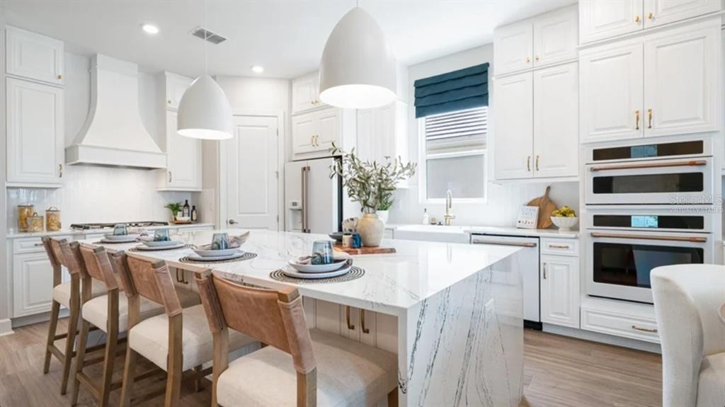 A bright white kitchen features a large marble-topped island with seating and stainless steel appliances — 7724 MOONBEAM AVENUE, SARASOTA, FL