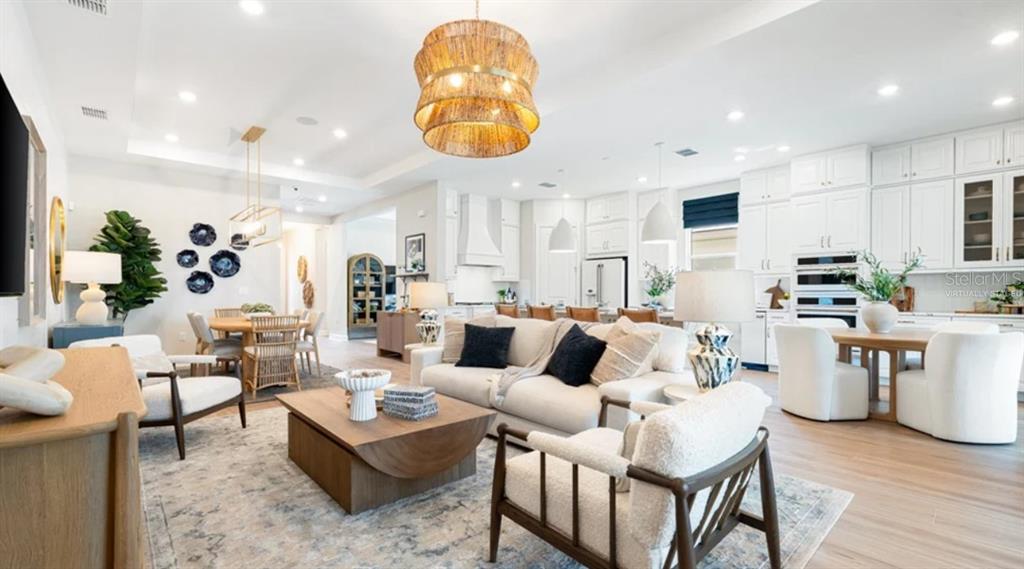 An open-concept living room and kitchen feature white cabinetry, a large chandelier, and neutral furniture — 7724 MOONBEAM AVENUE, SARASOTA, FL