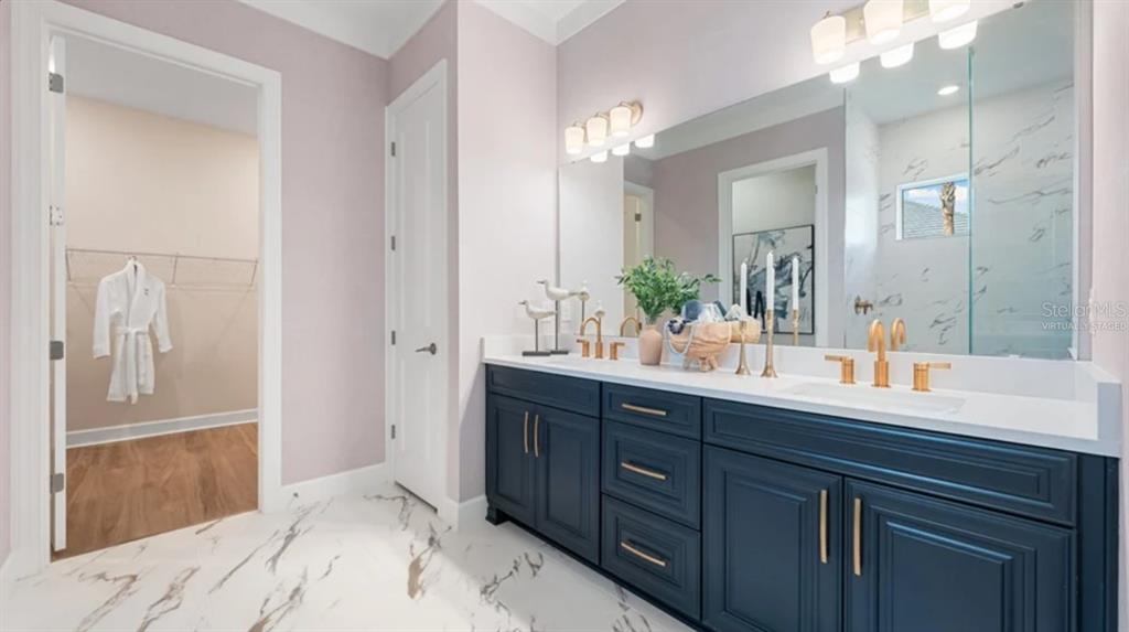 A bathroom features a double vanity with dark blue cabinets, gold hardware, and marble flooring — 7724 MOONBEAM AVENUE, SARASOTA, FL