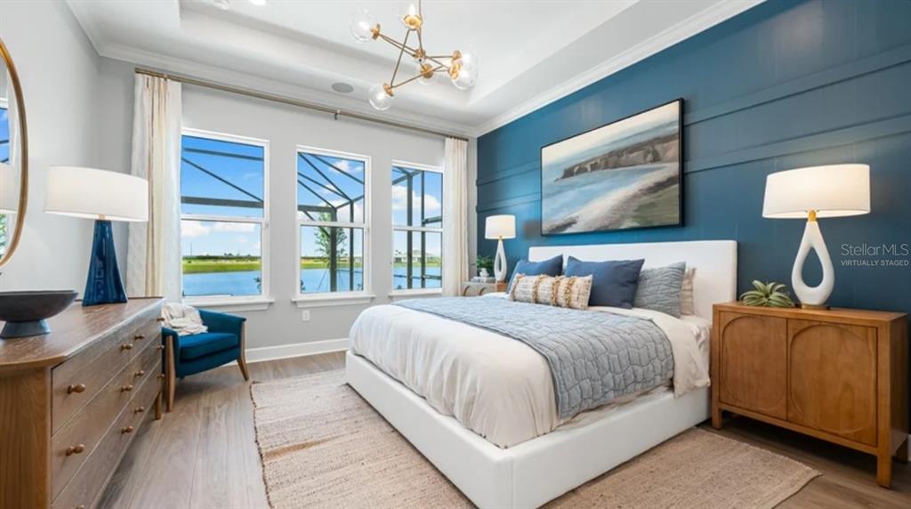 A bedroom features a blue accent wall, a white bed, and windows overlooking a lake — 7724 MOONBEAM AVENUE, SARASOTA, FL