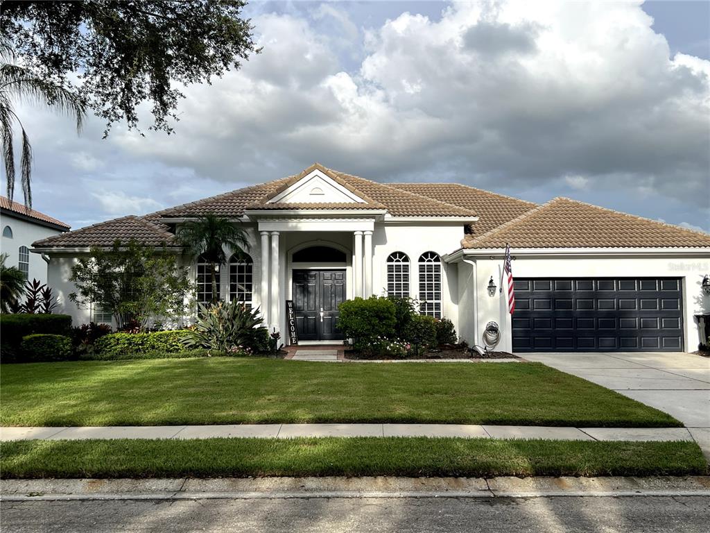 A single-story house with a tiled roof, white stucco exterior, and a dark garage door — 7555 TORI WAY, BRADENTON, FL