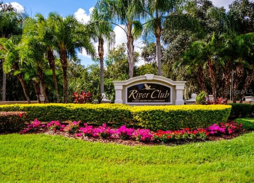 A sign for River Club stands behind a manicured hedge and vibrant pink flowers — 7555 TORI WAY, BRADENTON, FL