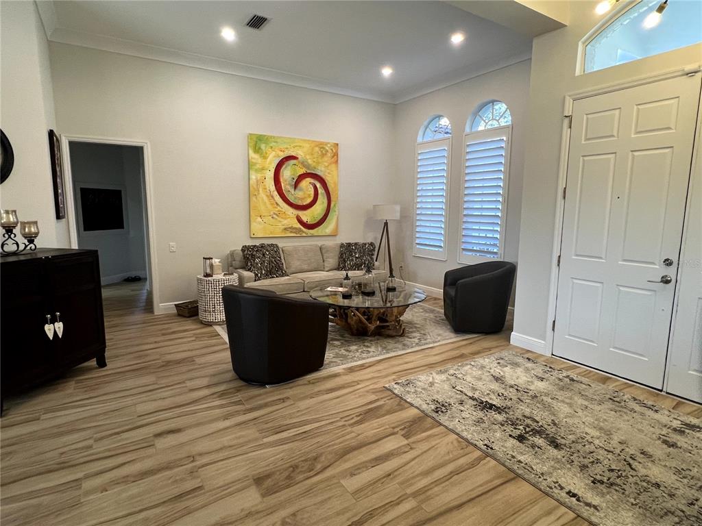 A living room features light wood-look flooring, a sofa, two armchairs, and a large abstract painting — 7555 TORI WAY, BRADENTON, FL