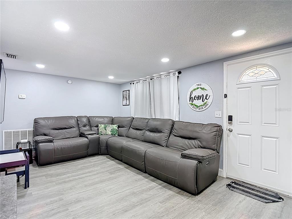A living room features a large gray sectional sofa, light wood flooring, and a white door — 5913 APPLETREE ROAD, HOLIDAY, FL