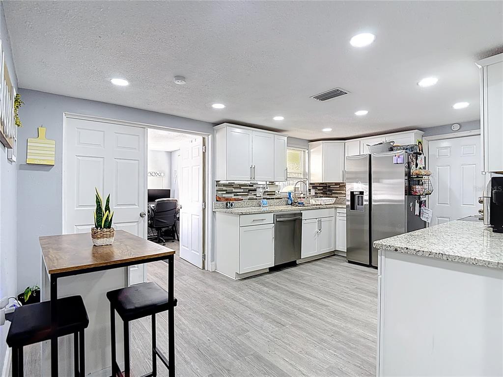 A kitchen features white cabinets, granite countertops, stainless steel appliances, and a small dining table — 5913 APPLETREE ROAD, HOLIDAY, FL