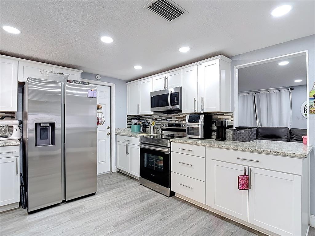 A kitchen features white cabinets, stainless steel appliances, granite countertops, and light wood-look flooring — 5913 APPLETREE ROAD, HOLIDAY, FL