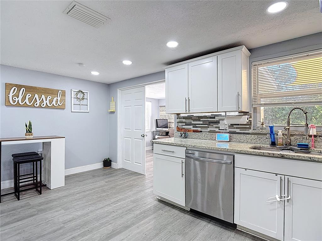A kitchen features white cabinets, stainless steel appliances, granite countertops, and light gray flooring — 5913 APPLETREE ROAD, HOLIDAY, FL
