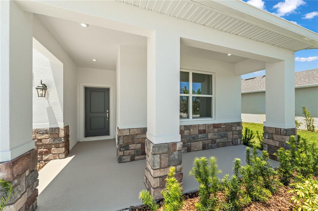 A covered front porch with stone accents, white columns, and a dark gray front door — 12837 TROVITA DRIVE, GRAND ISLAND, FL