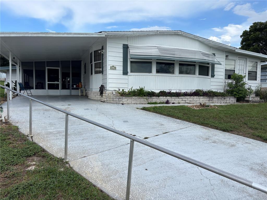 A white mobile home features a metal carport, a screened porch, and a brick planter — 3438 BANBERRY CIRCLE UNIT 1790, ZELLWOOD, FL