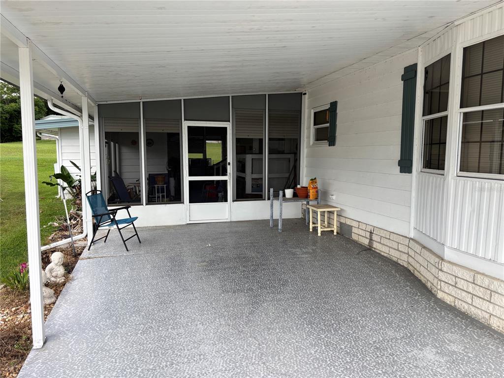 A covered concrete patio features a screened-in porch entrance and a blue folding chair — 3438 BANBERRY CIRCLE UNIT 1790, ZELLWOOD, FL