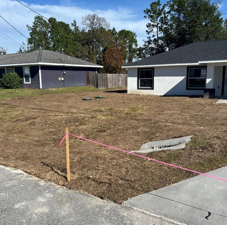 A view of a residential front yard with a concrete drainage inlet and survey stakes — 24492 NW HEMLOCK AVENUE, DUNNELLON, FL
