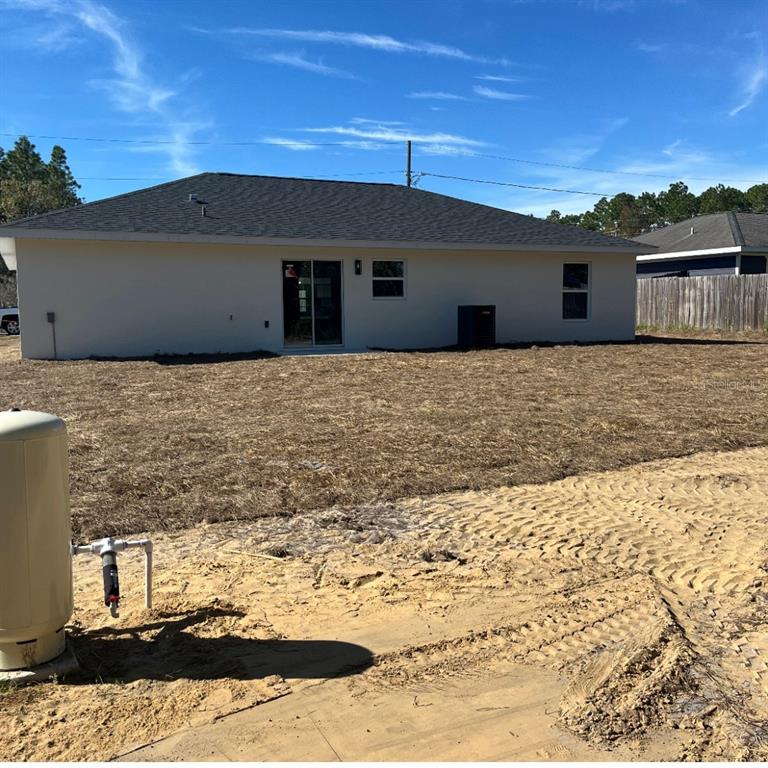 The exterior rear view of a single-story house features a tan stucco finish and yard — 24492 NW HEMLOCK AVENUE, DUNNELLON, FL