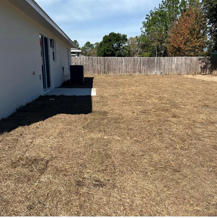 A view of a house exterior with a sliding glass door and a dry, grassy yard — 24492 NW HEMLOCK AVENUE, DUNNELLON, FL
