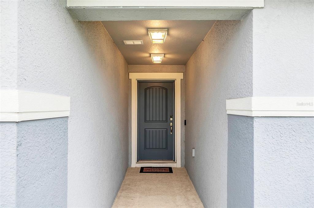 A recessed entryway features a dark blue front door, two ceiling lights, and stucco walls — 1877 RIVER CREST AVENUE, ST CLOUD, FL