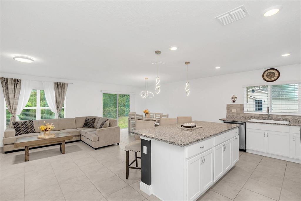 An open-concept living room and kitchen feature tile floors, a granite island, and neutral furniture — 1877 RIVER CREST AVENUE, ST CLOUD, FL