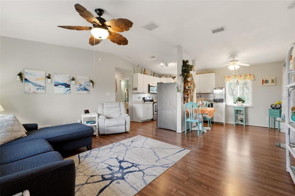 An open-concept living room and kitchen featuring wood-look flooring, a ceiling fan, and blue furniture — 10182 GULFSTREAM BOULEVARD, ENGLEWOOD, FL