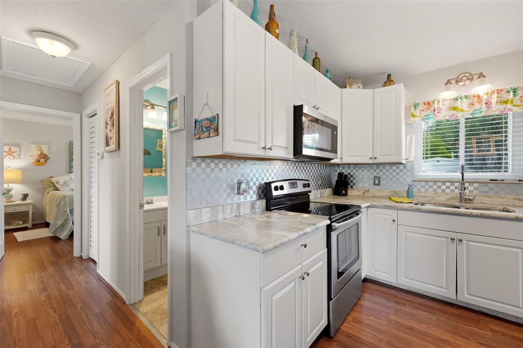 A kitchen with white cabinets, stainless steel appliances, and a checkered backsplash next to a hallway — 10182 GULFSTREAM BOULEVARD, ENGLEWOOD, FL