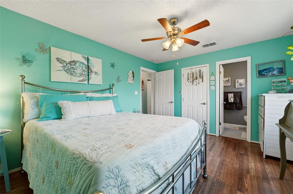 A bedroom features teal walls, a metal bed frame, a ceiling fan, and wood flooring — 10182 GULFSTREAM BOULEVARD, ENGLEWOOD, FL