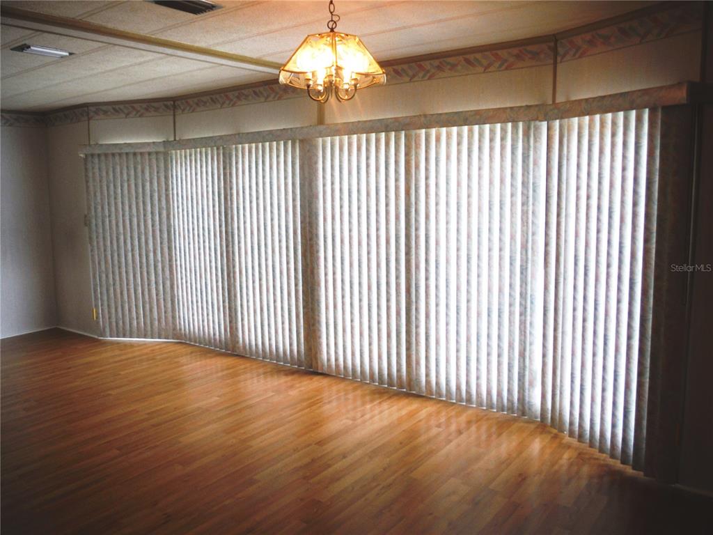 A room with wood-look flooring, a hanging light fixture, and floor-to-ceiling vertical window blinds — 30 STAG RUN COURT UNIT 11, SAFETY HARBOR, FL