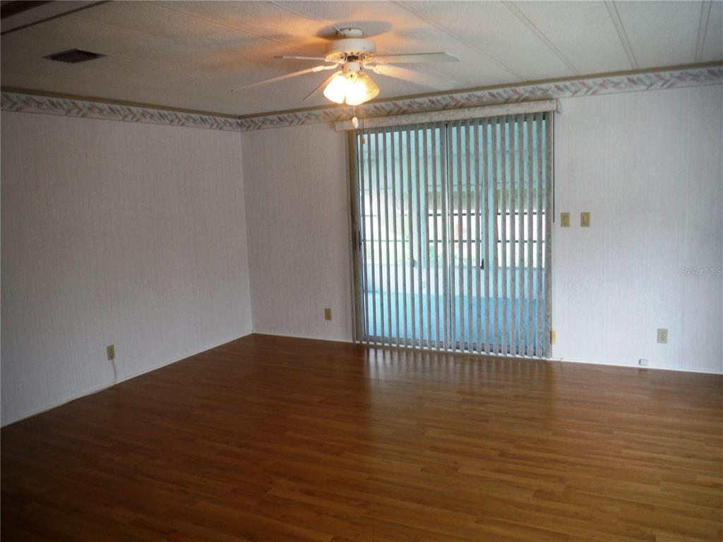 An empty room features wood-look flooring, white walls with a border, and vertical sliding blinds — 30 STAG RUN COURT UNIT 11, SAFETY HARBOR, FL
