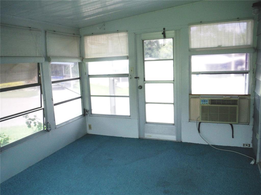 A sunroom with blue carpeting, white walls, multiple windows, and a window-mounted air conditioner — 30 STAG RUN COURT UNIT 11, SAFETY HARBOR, FL