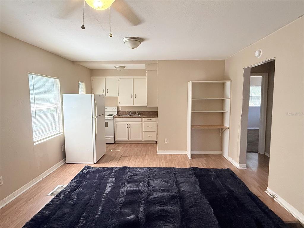 A kitchen with white cabinets, a refrigerator, and wood-look flooring opens to a living area — 986 22ND AVENUE S UNIT 3, ST PETERSBURG, FL