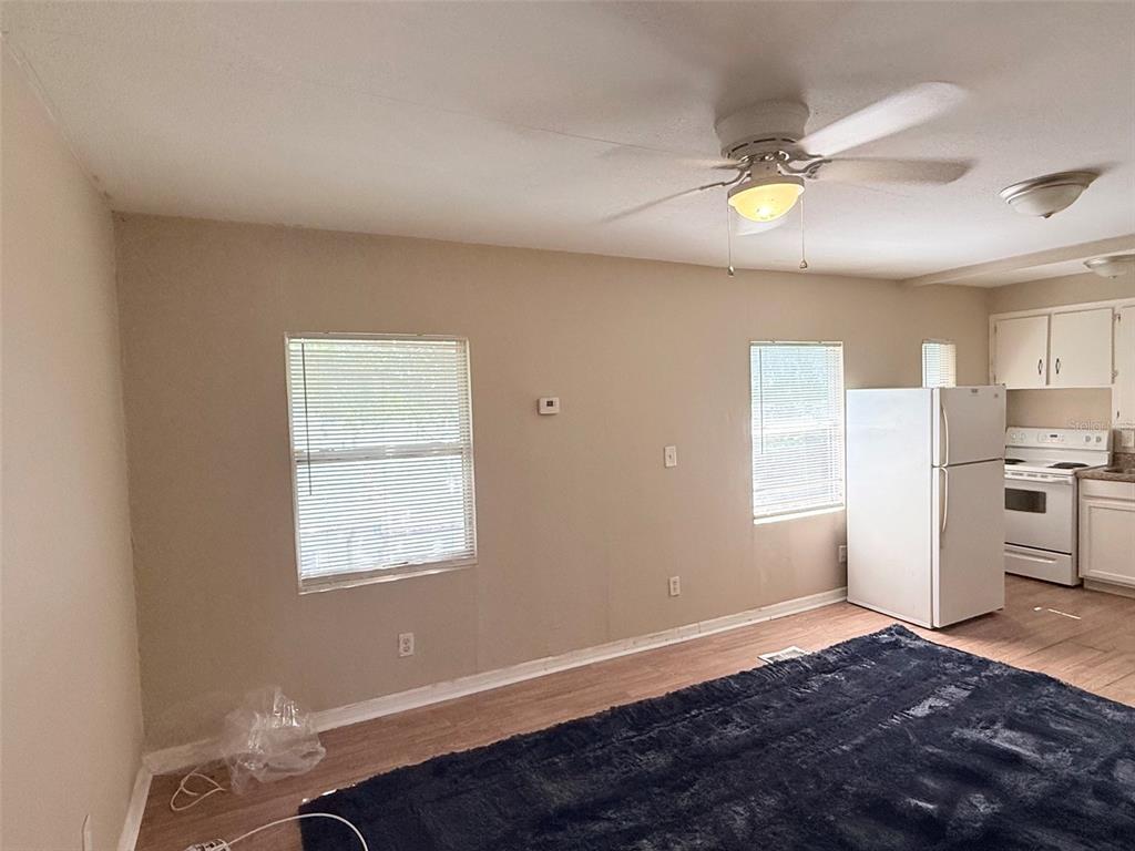 An empty room features wood-look flooring, beige walls, a ceiling fan, and a white door — 986 22ND AVENUE S UNIT 3, ST PETERSBURG, FL