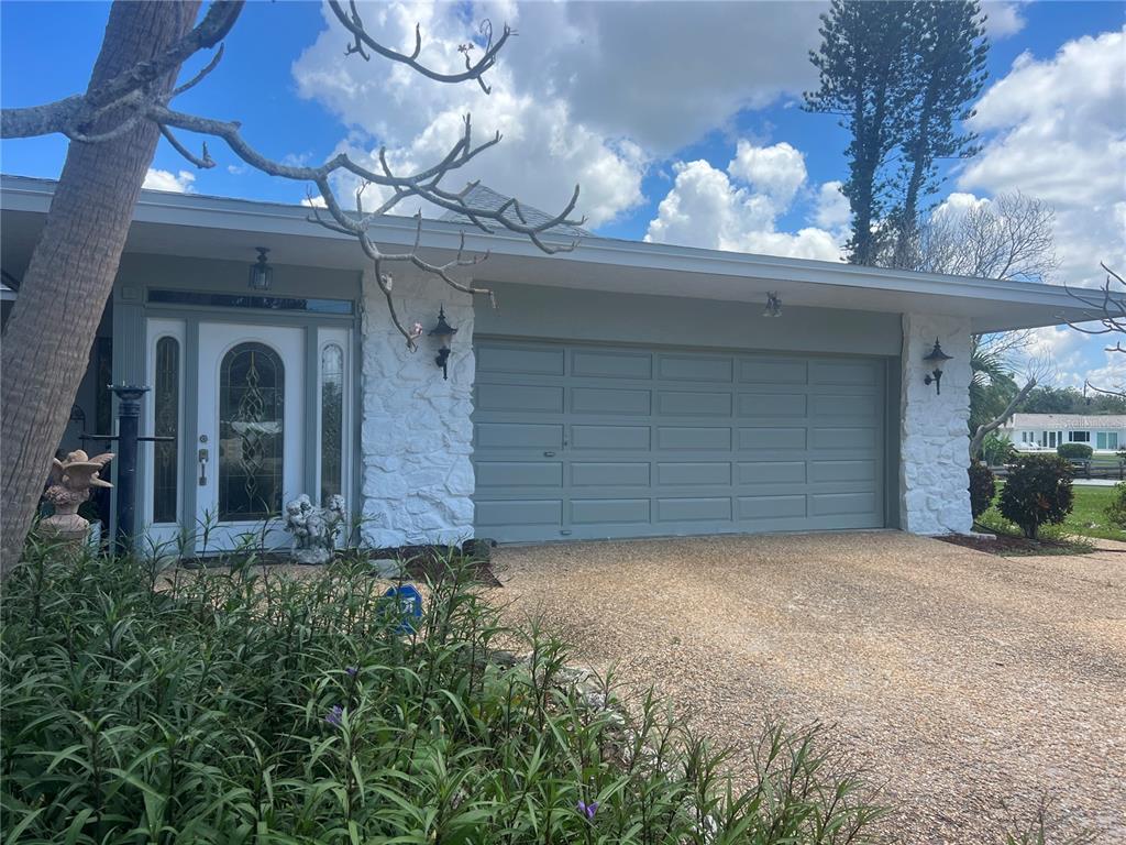 A single-story house exterior features a white stone facade, a gray garage door, and a front entrance — 6937 MIDNIGHT PASS ROAD, SARASOTA, FL
