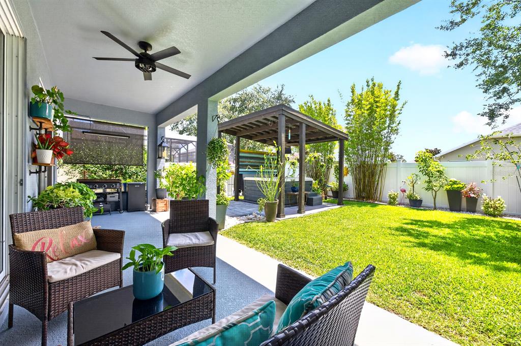 A covered patio with wicker furniture overlooks a backyard featuring a pergola and hot tub — 1135 TOLUKE POINT, ORLANDO, FL