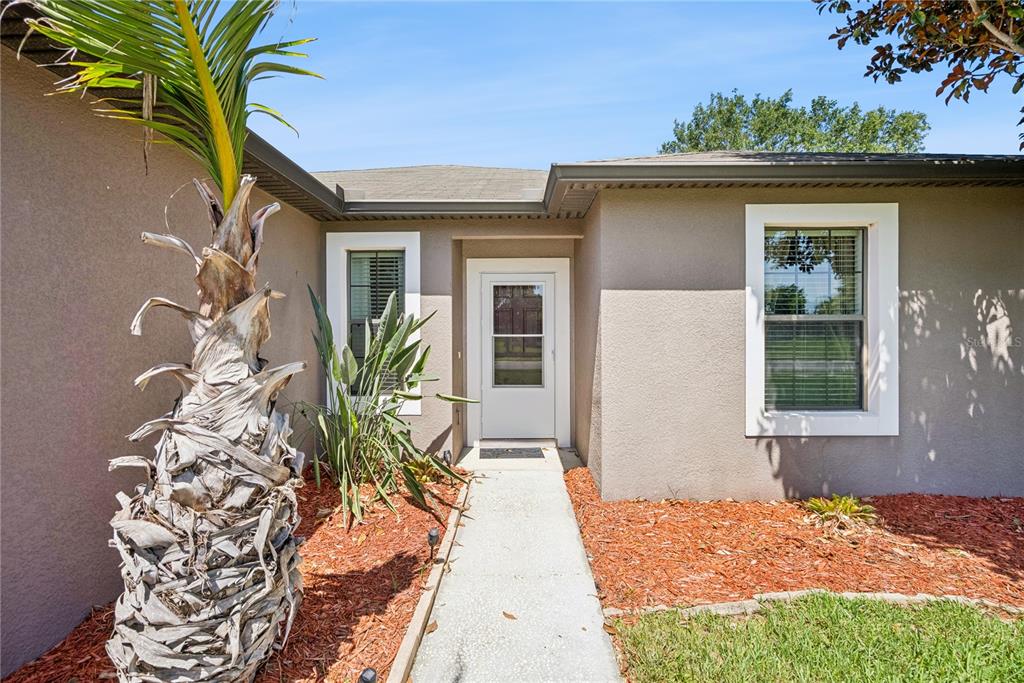 A concrete walkway leads to the front entrance of a tan house with a palm tree — 2440 VINEYARD CIRCLE, SANFORD, FL