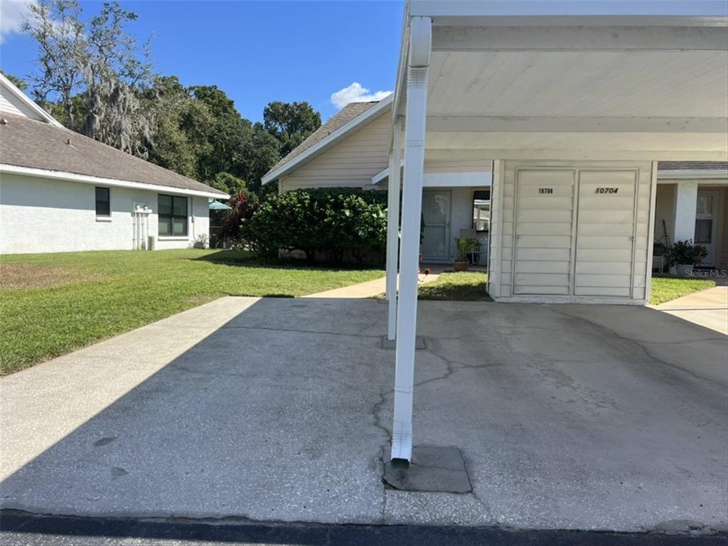 A concrete driveway leads to a covered carport attached to a single-story residential building — 10706 LAQUINTA DRIVE, NEW PORT RICHEY, FL