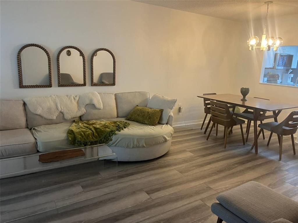 A living and dining area with a curved sectional sofa, wood-look flooring, and three arched mirrors — 10706 LAQUINTA DRIVE, NEW PORT RICHEY, FL