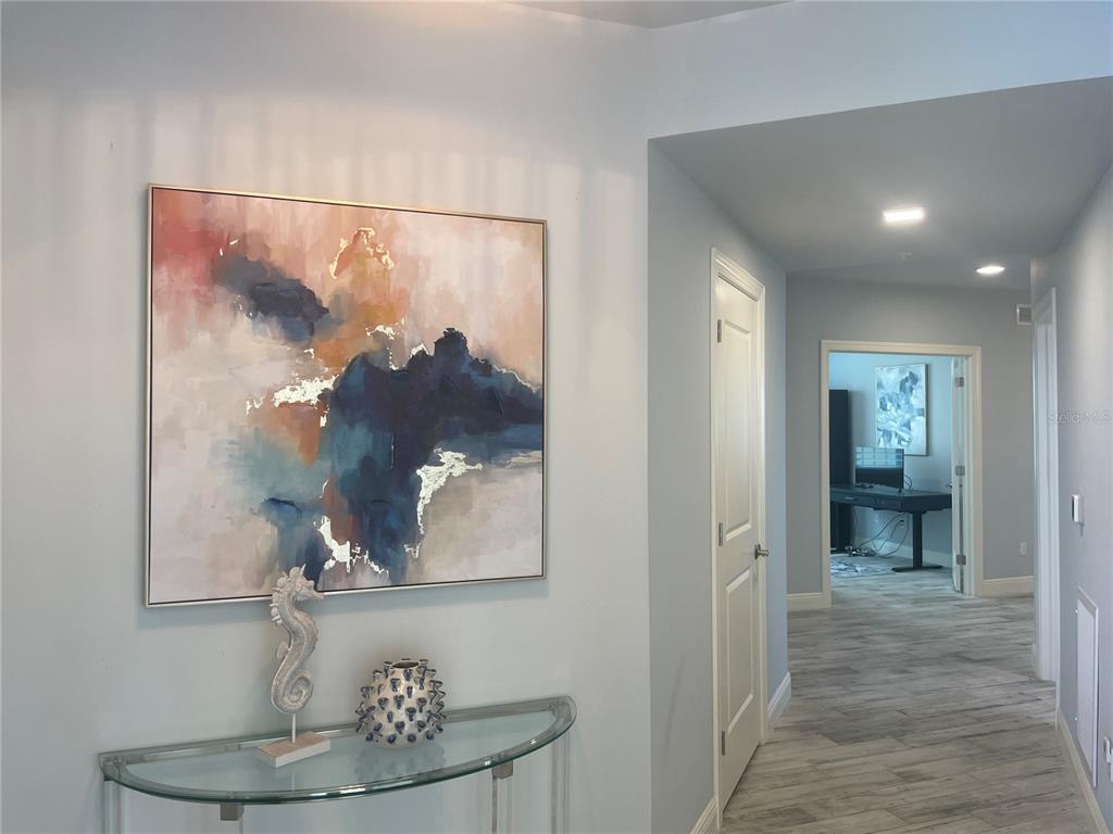 A hallway features a glass console table, abstract wall art, and a view into an office — 260 HIDDEN BAY DRIVE UNIT 401, OSPREY, FL