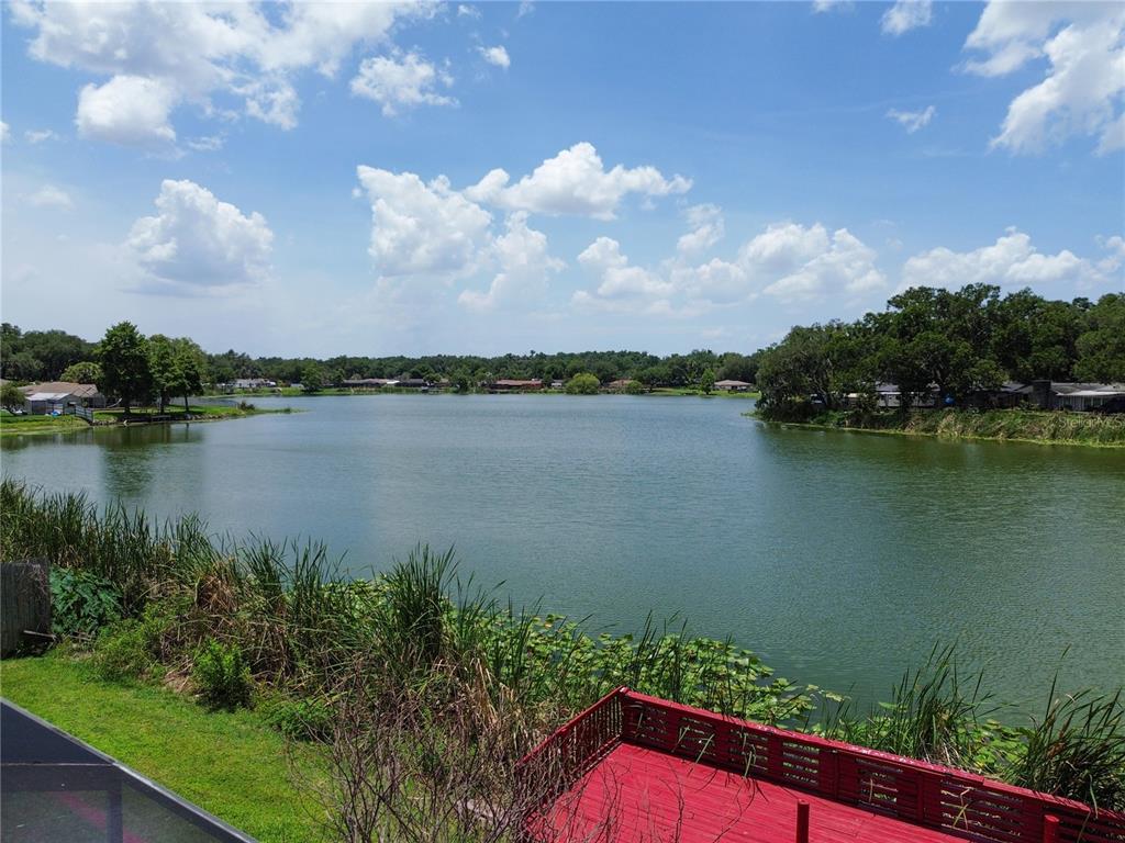 A view of a lake from a red wooden deck with surrounding trees and vegetation — 912 SHANGRI LA DRIVE, SEFFNER, FL