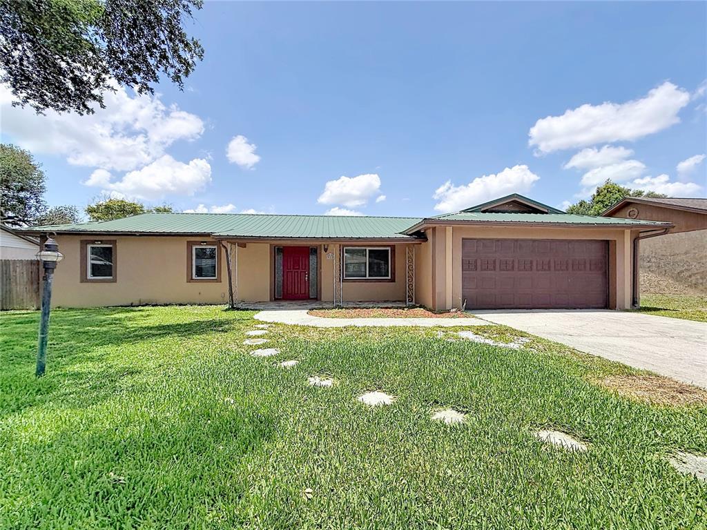 A single-story house with a green metal roof, tan stucco exterior, and attached garage — 912 SHANGRI LA DRIVE, SEFFNER, FL