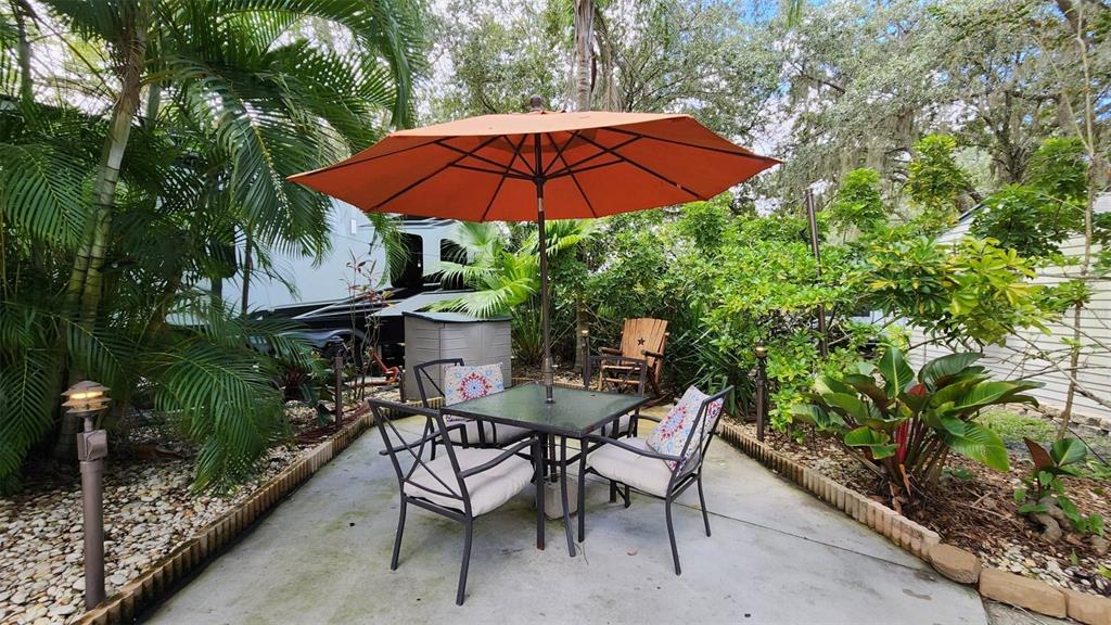 A patio with a table, chairs, and an orange umbrella sits beside a parked RV — 153 HORSESHOE BEND, RIVER RANCH, FL