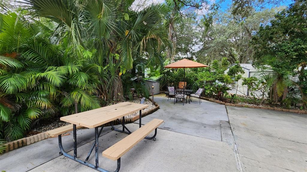 A concrete patio features a picnic table, a dining set with an umbrella, and landscaping — 153 HORSESHOE BEND, RIVER RANCH, FL