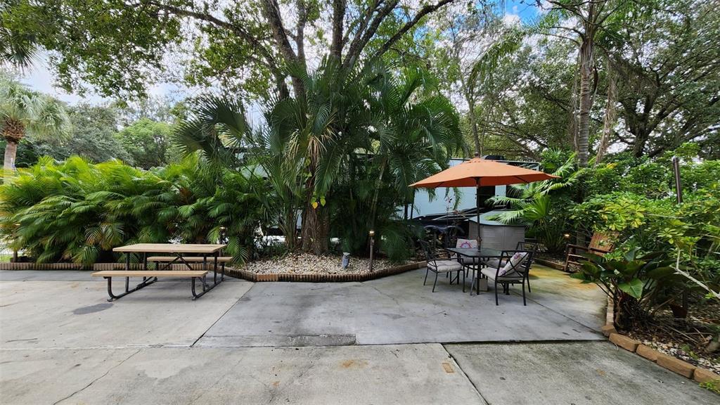 A concrete patio features a picnic table, a dining set with an umbrella, and landscaping — 153 HORSESHOE BEND, RIVER RANCH, FL