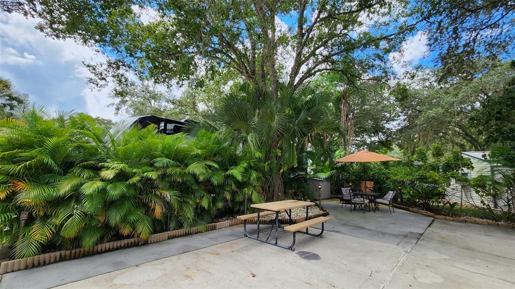 A concrete patio features a picnic table, a dining set with an umbrella, and lush landscaping — 153 HORSESHOE BEND, RIVER RANCH, FL