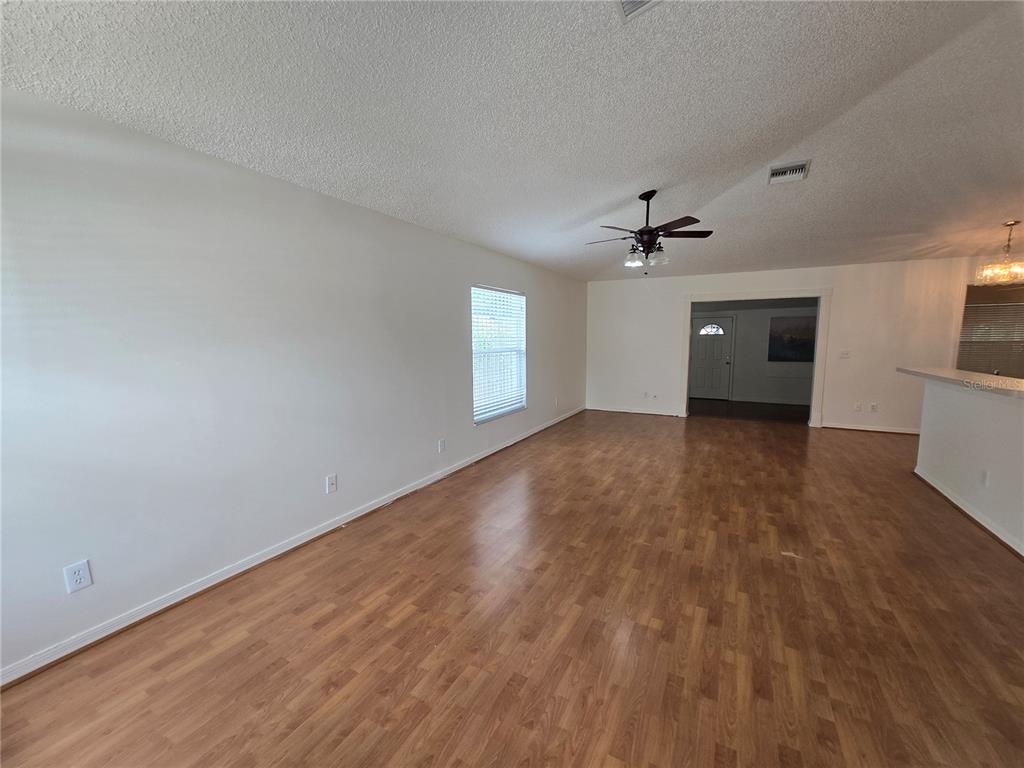 An open-concept living area features wood-look flooring, a vaulted ceiling, and an adjoining kitchen — 1926 29TH AVENUE N, ST PETERSBURG, FL