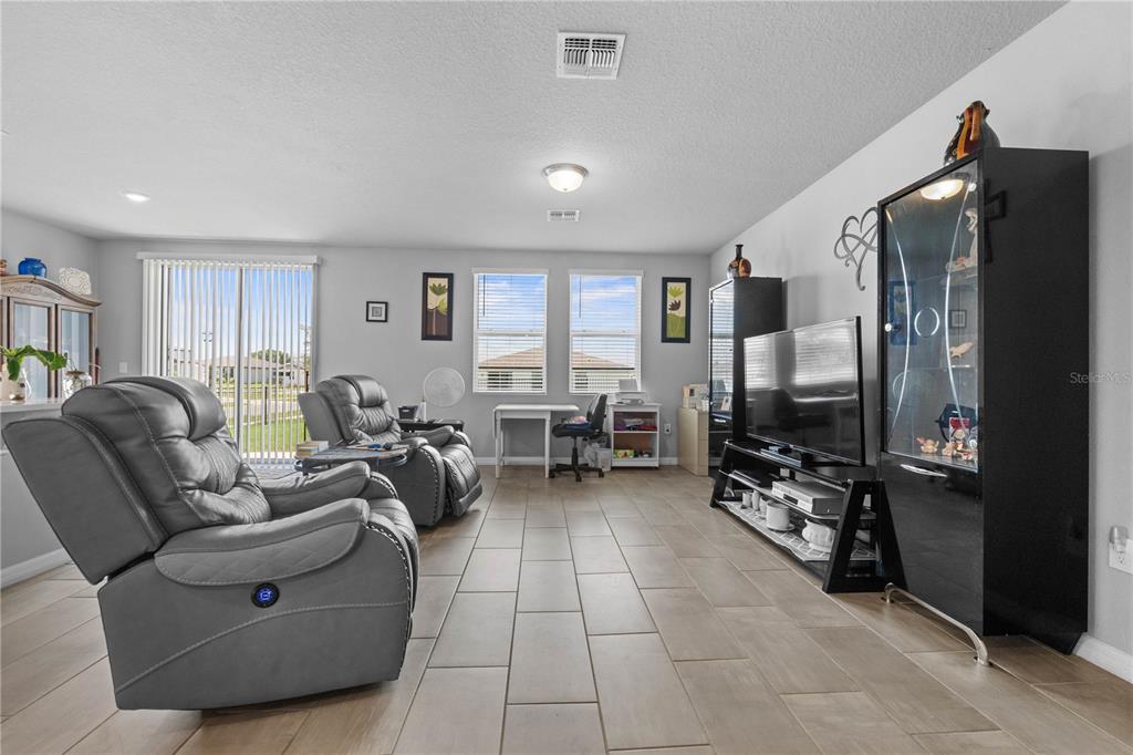 A living room features gray tile flooring, two leather recliners, a television, and a display cabinet — 1502 BRANCHWOOD LANE, AUBURNDALE, FL