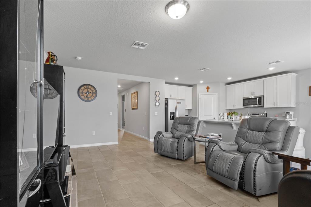 A living room with gray walls, tile flooring, and two gray recliners facing a kitchen — 1502 BRANCHWOOD LANE, AUBURNDALE, FL